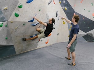 a couple of men standing next to each other on a climbing wall