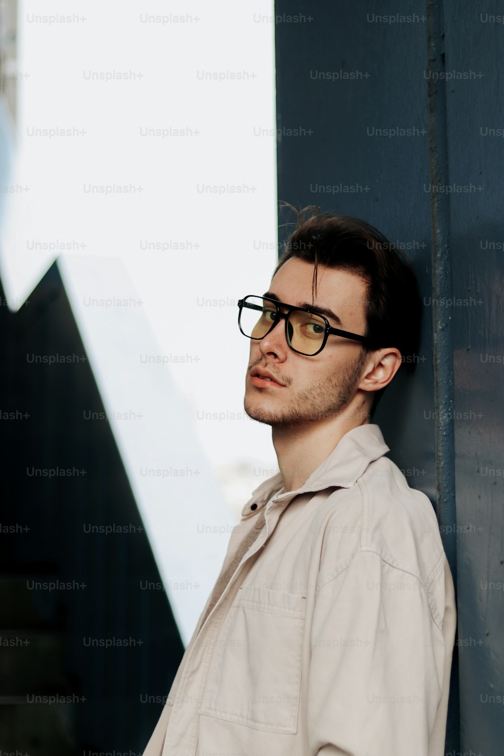 a man wearing glasses leaning against a wall