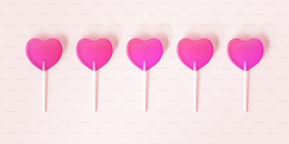 uma fileira de pirulitos em forma de coração em um fundo rosa