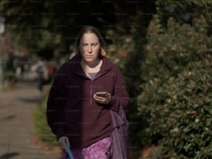 Una mujer caminando por una acera con un teléfono celular en la mano