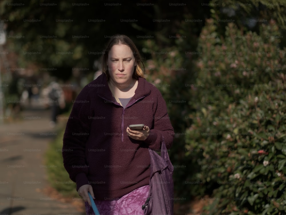 a woman walking down a sidewalk with a cell phone in her hand