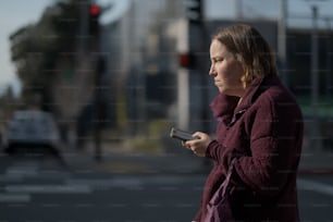 uma mulher em pé em uma esquina olhando para seu telefone celular