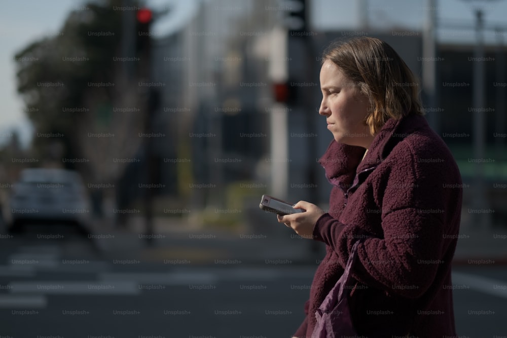 Una donna in piedi all'angolo di una strada che guarda il suo cellulare