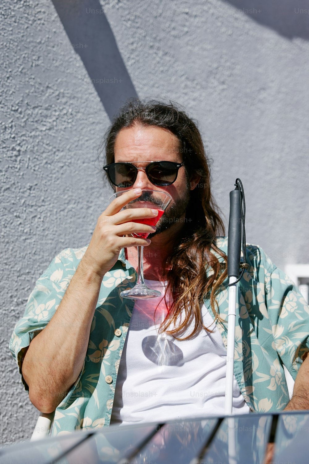 긴 머리와 선글라스를 쓴 남자가 와인 잔��을 마시고 있다