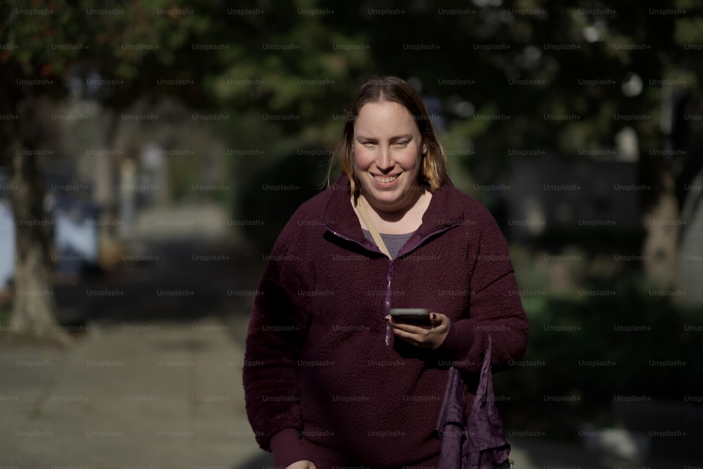 uma mulher andando por uma rua segurando um telefone celular