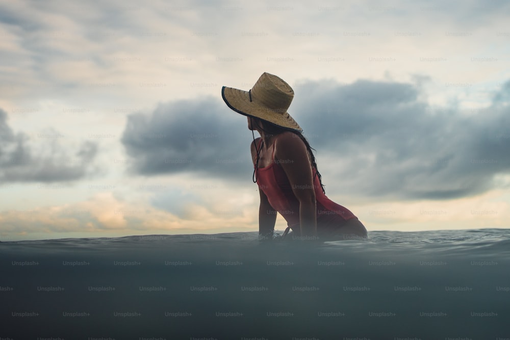 Una mujer con sombrero sentada en una tabla de surf en el océano