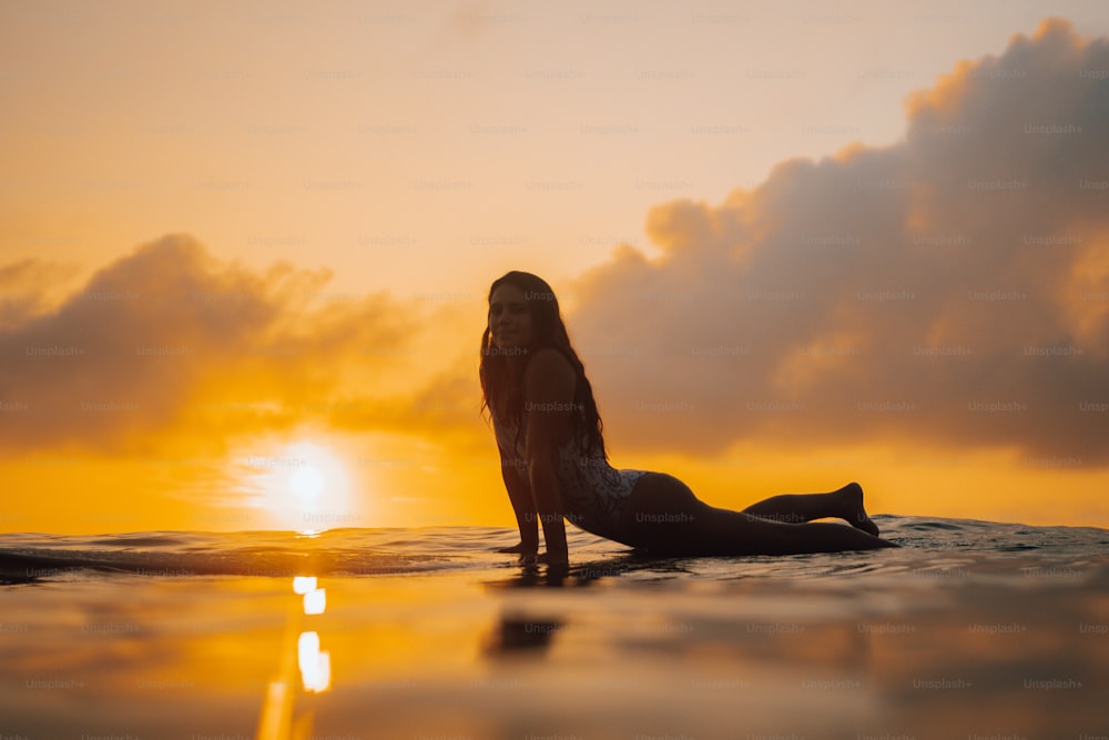 a woman laying on a surfboard in the ocean at sunset