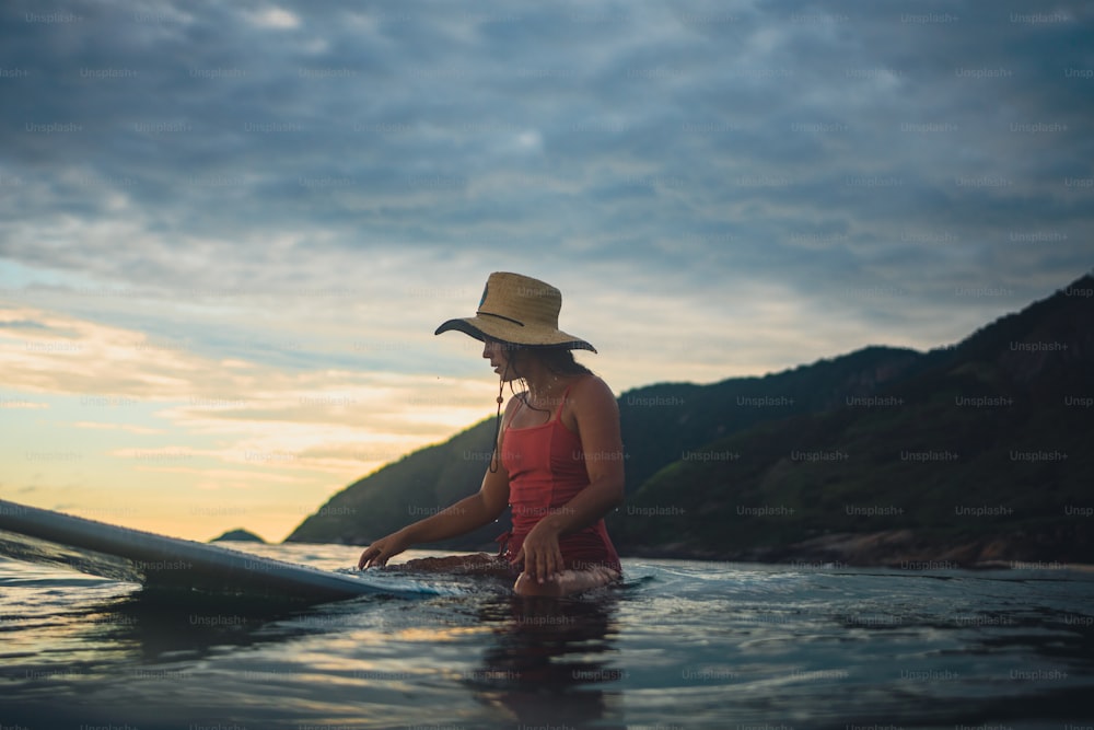 uma mulher em um chapéu está sentada em uma prancha de surf