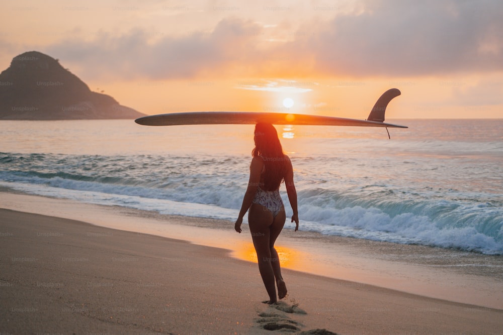 Una mujer caminando por la playa con una tabla de surf en la cabeza