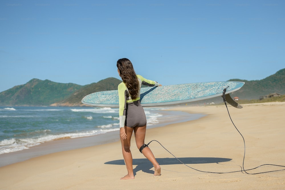 한 여자가 해변에서 서핑 보드를 들고 있다