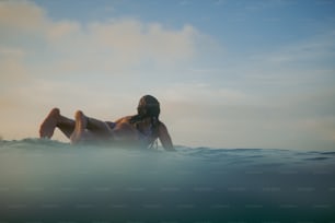 uma mulher deitada em cima de uma prancha de surf no oceano