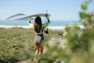 a woman carrying a surfboard on top of a lush green field
