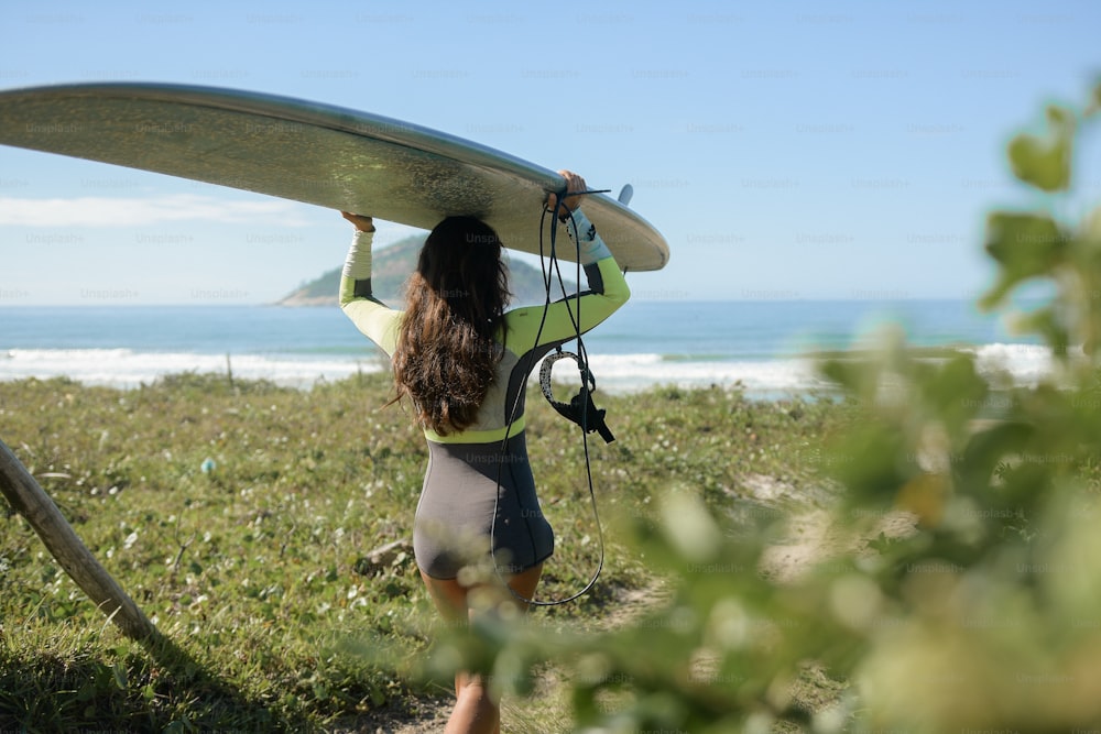 Une femme portant une planche de surf au sommet d’un champ verdoyant
