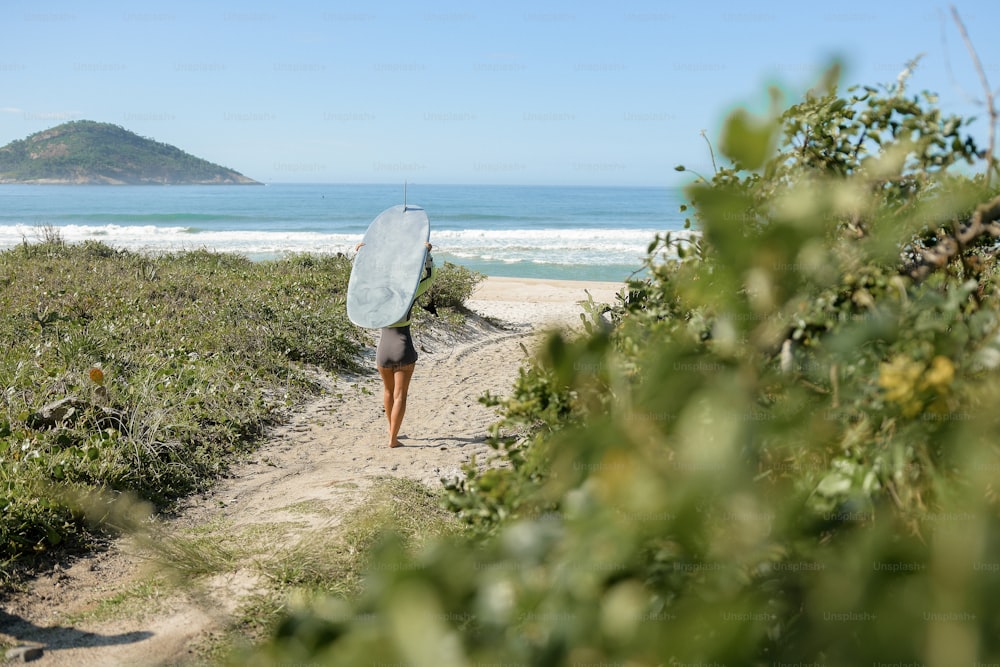uma pessoa andando por um caminho com uma prancha de surf