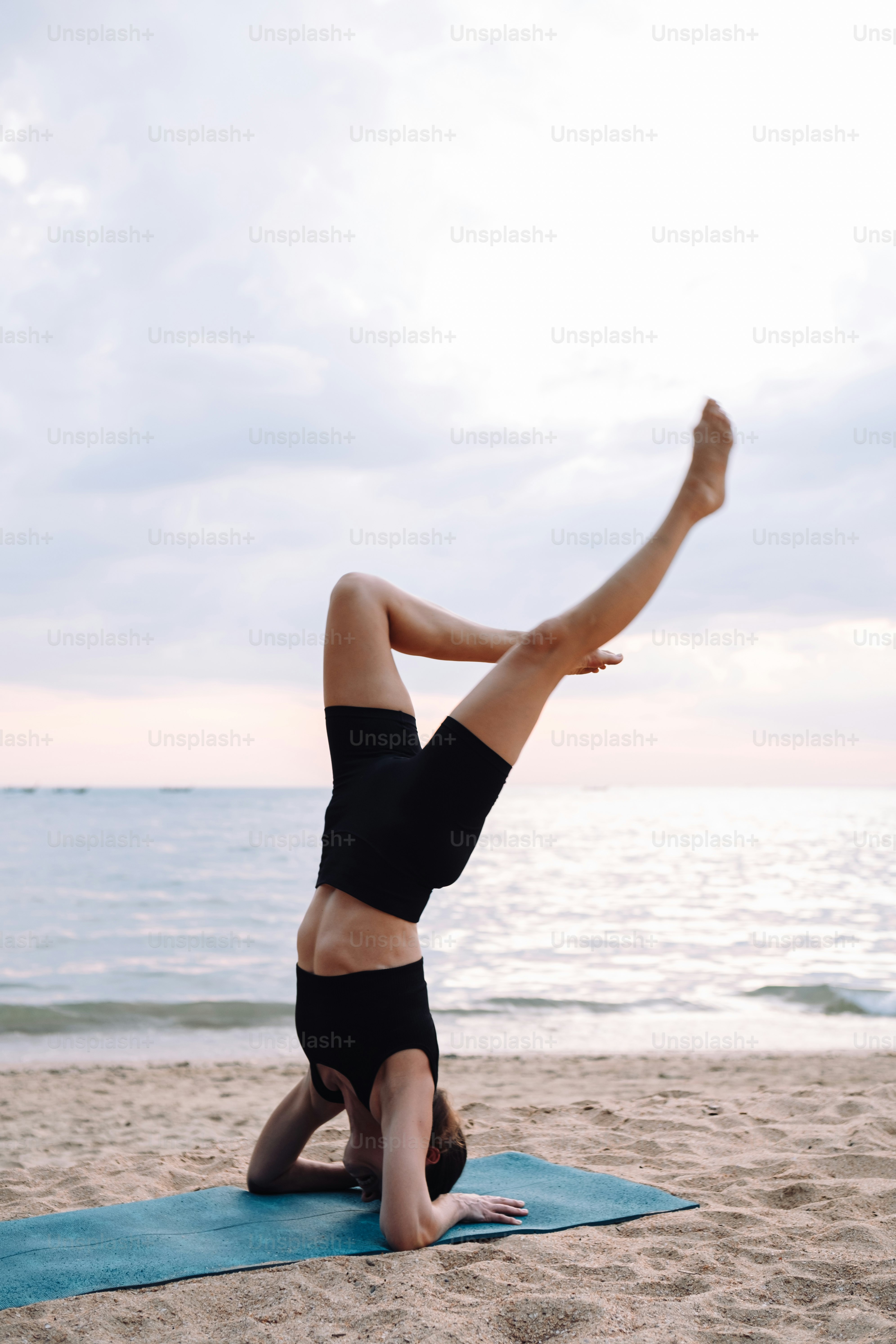 a woman doing a handstand on a towel on the beach
