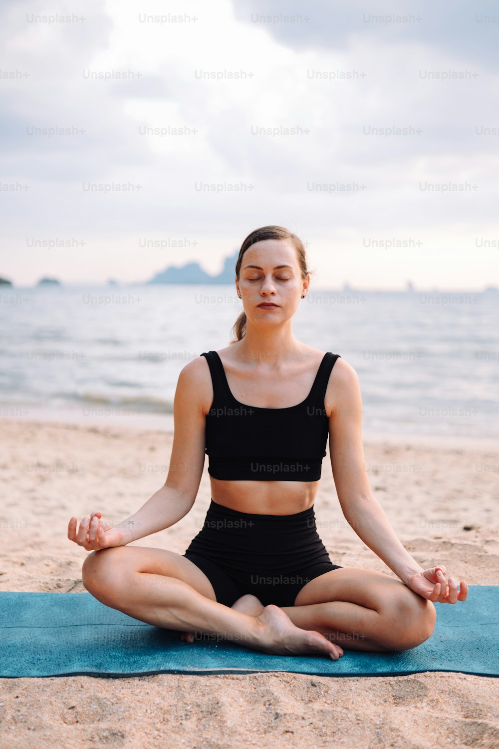 a woman sitting in a yoga position on the beach