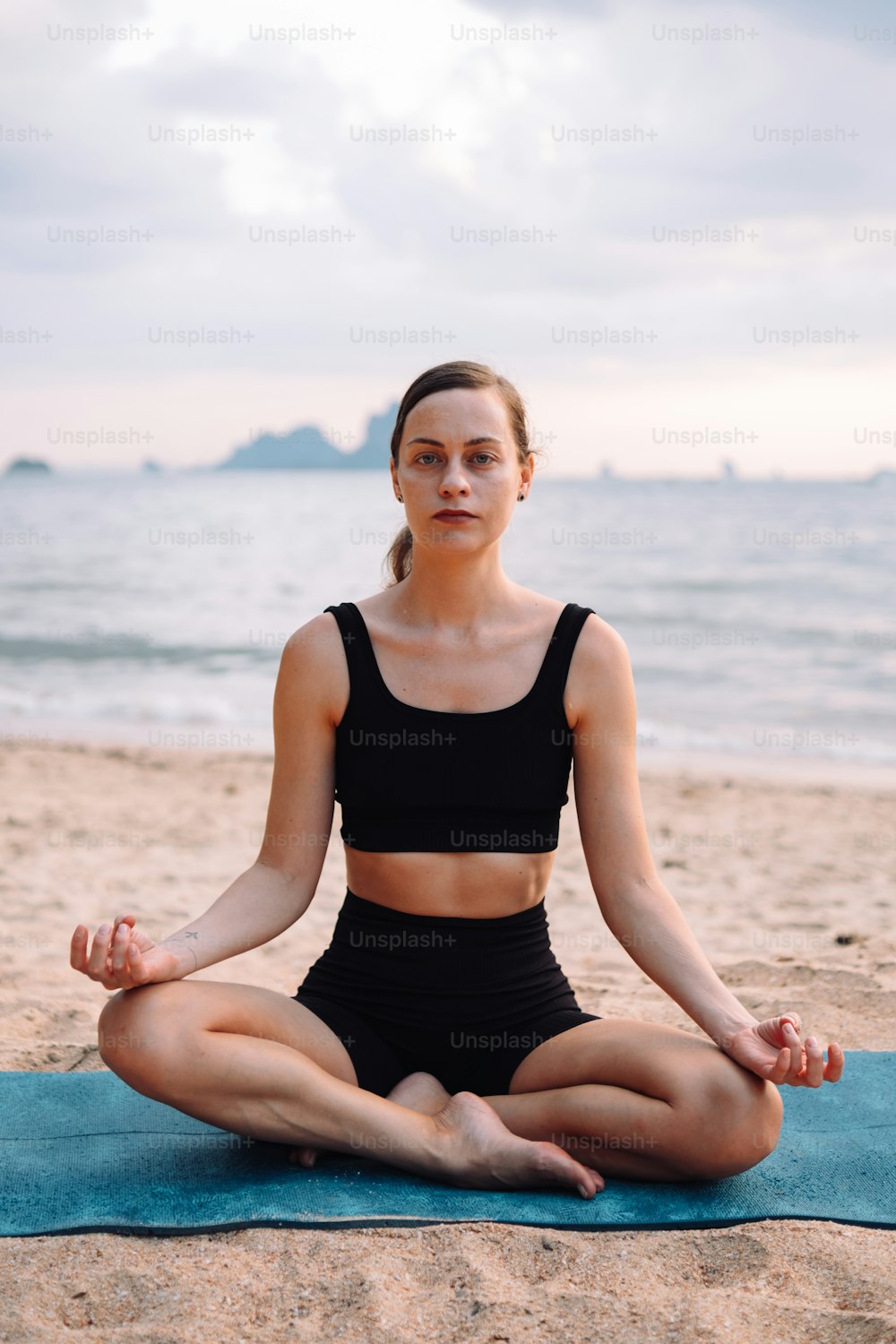 Una mujer sentada en una posición de yoga en la playa