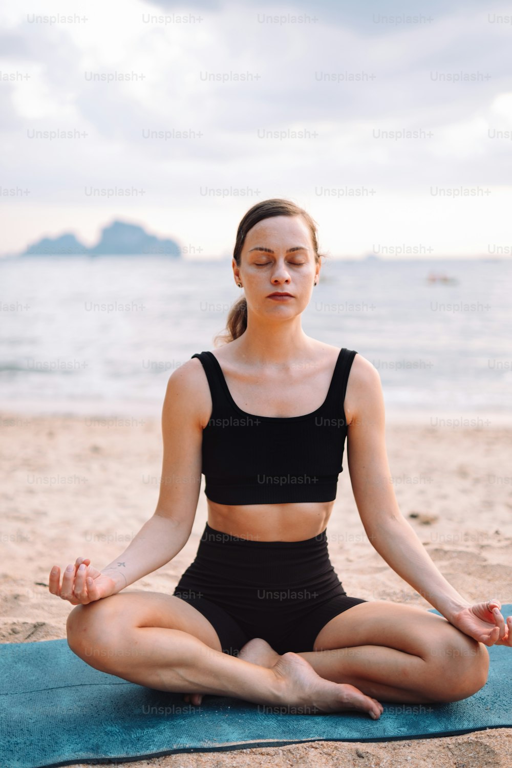 Eine Frau sitzt in einer Yoga-Position am Strand