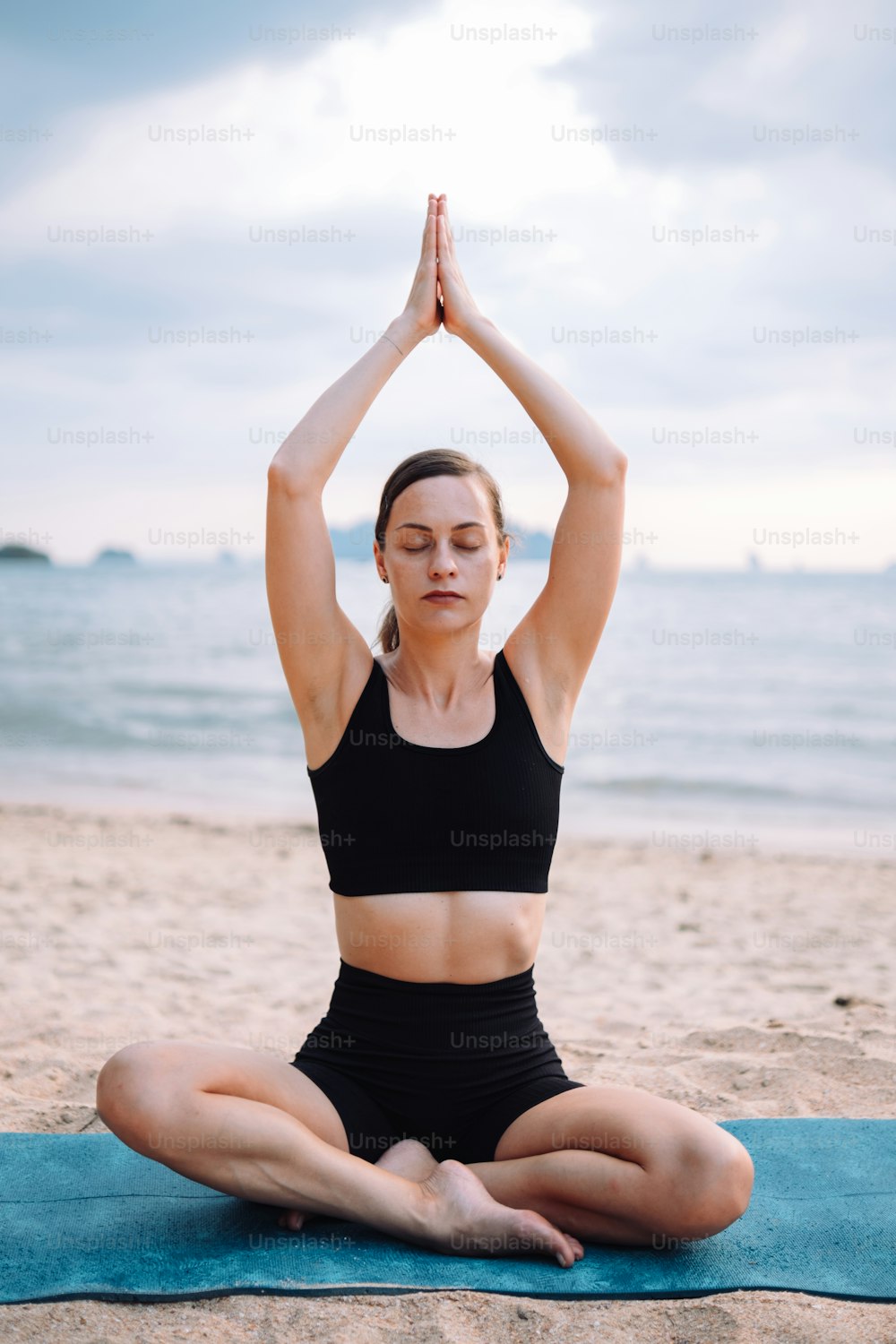 uma mulher sentada em uma posição de ioga na praia