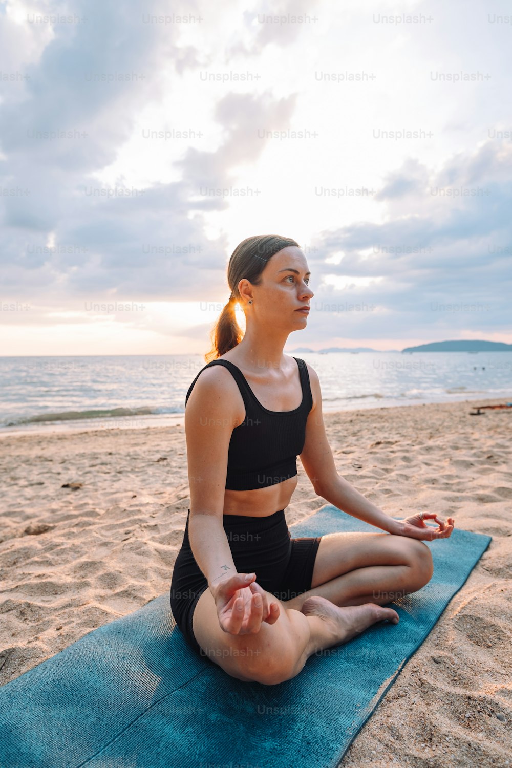 a woman sitting in a yoga position on a towel on the beach