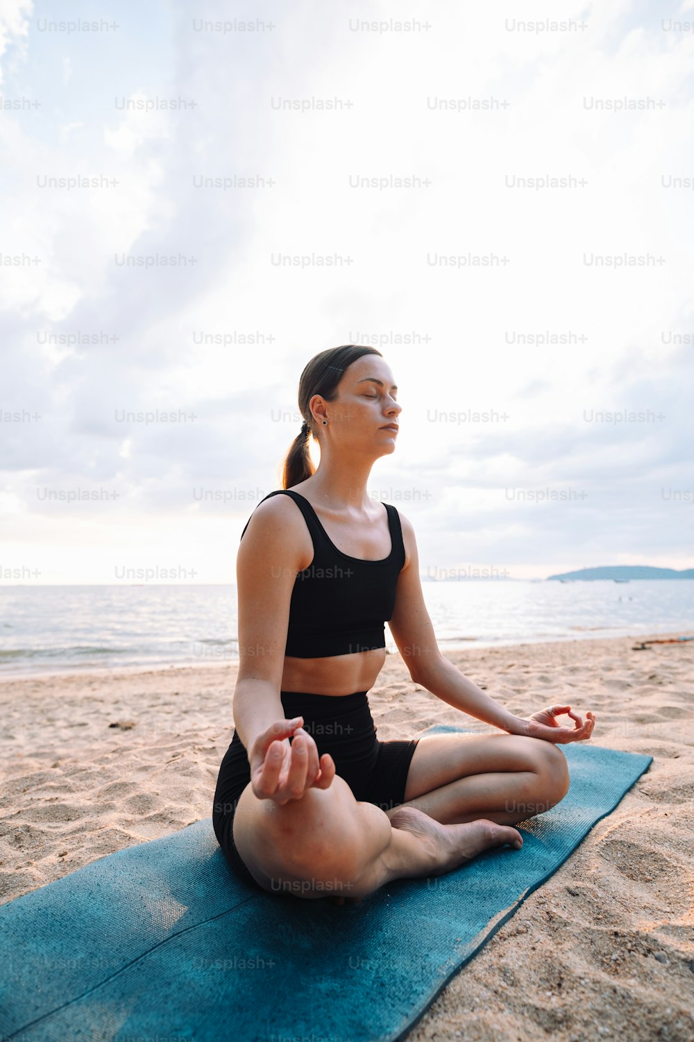 a woman sitting on a yoga mat on the beach
