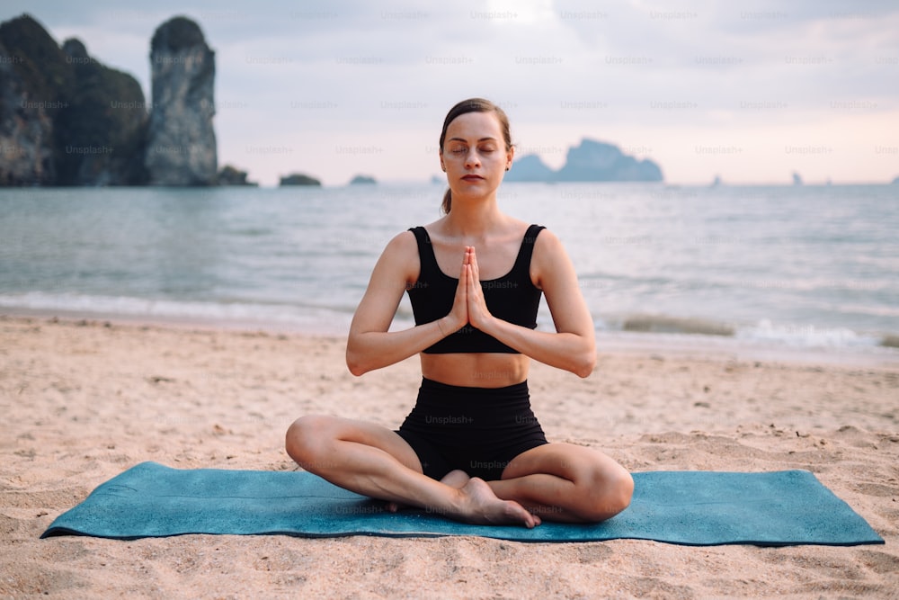 una donna seduta in una posizione yoga sulla spiaggia