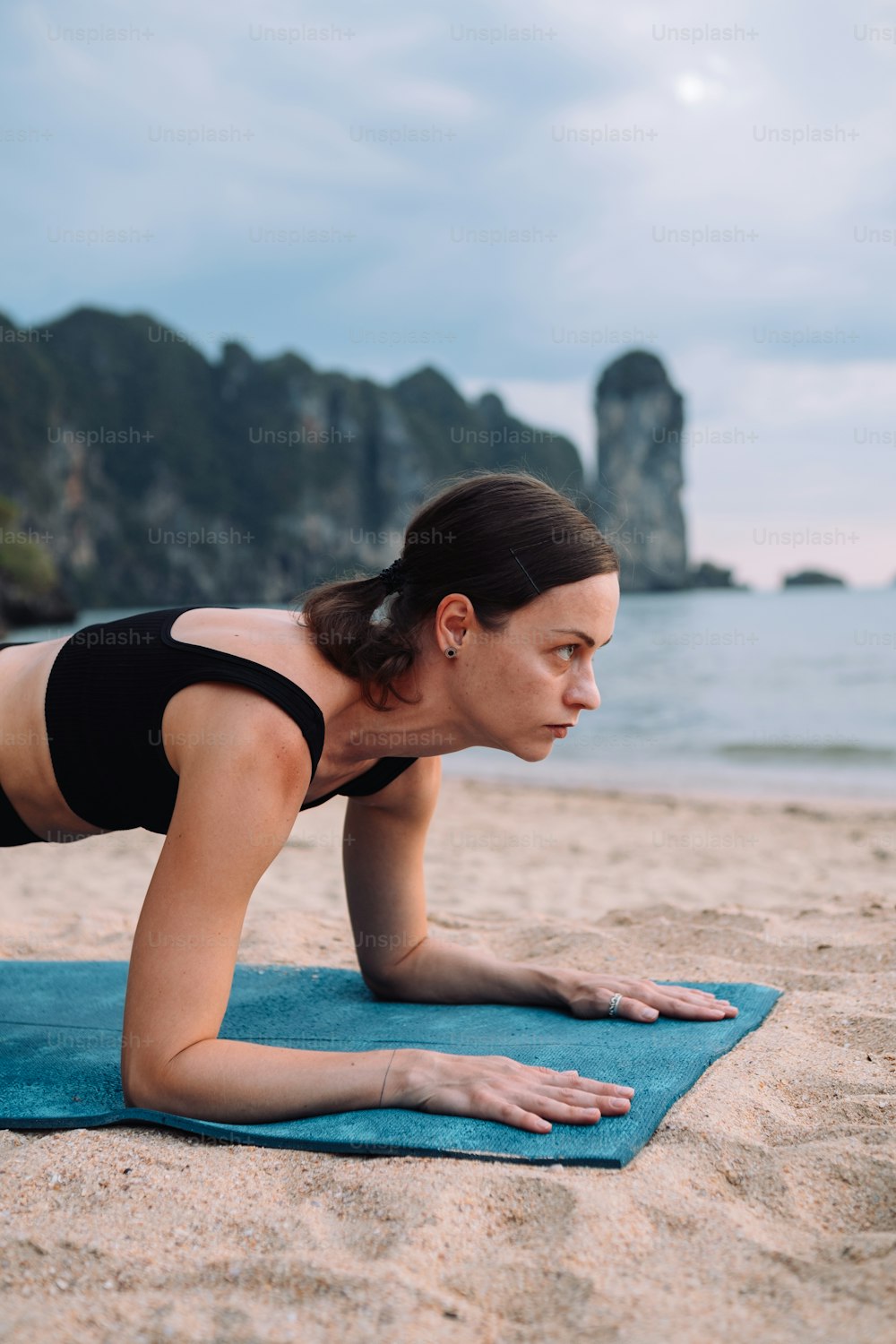 a woman doing push ups on a towel on the beach