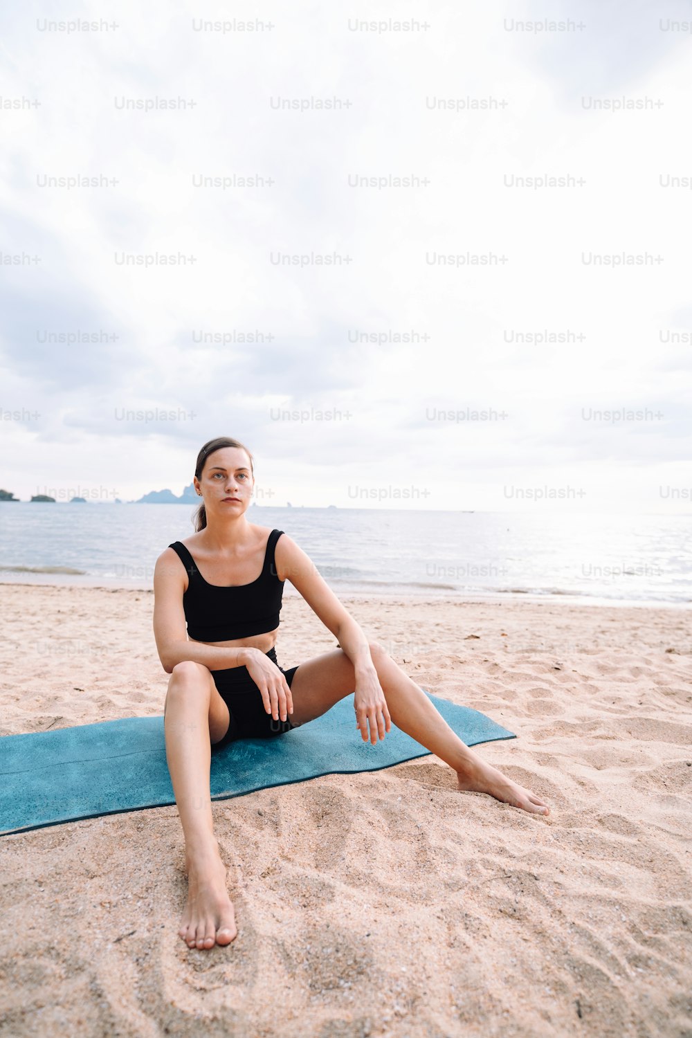a woman sitting on top of a blue mat on a beach