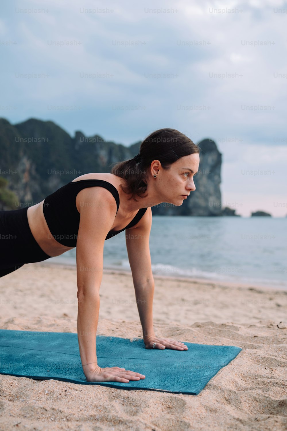 a woman is doing a push up on a towel on the beach