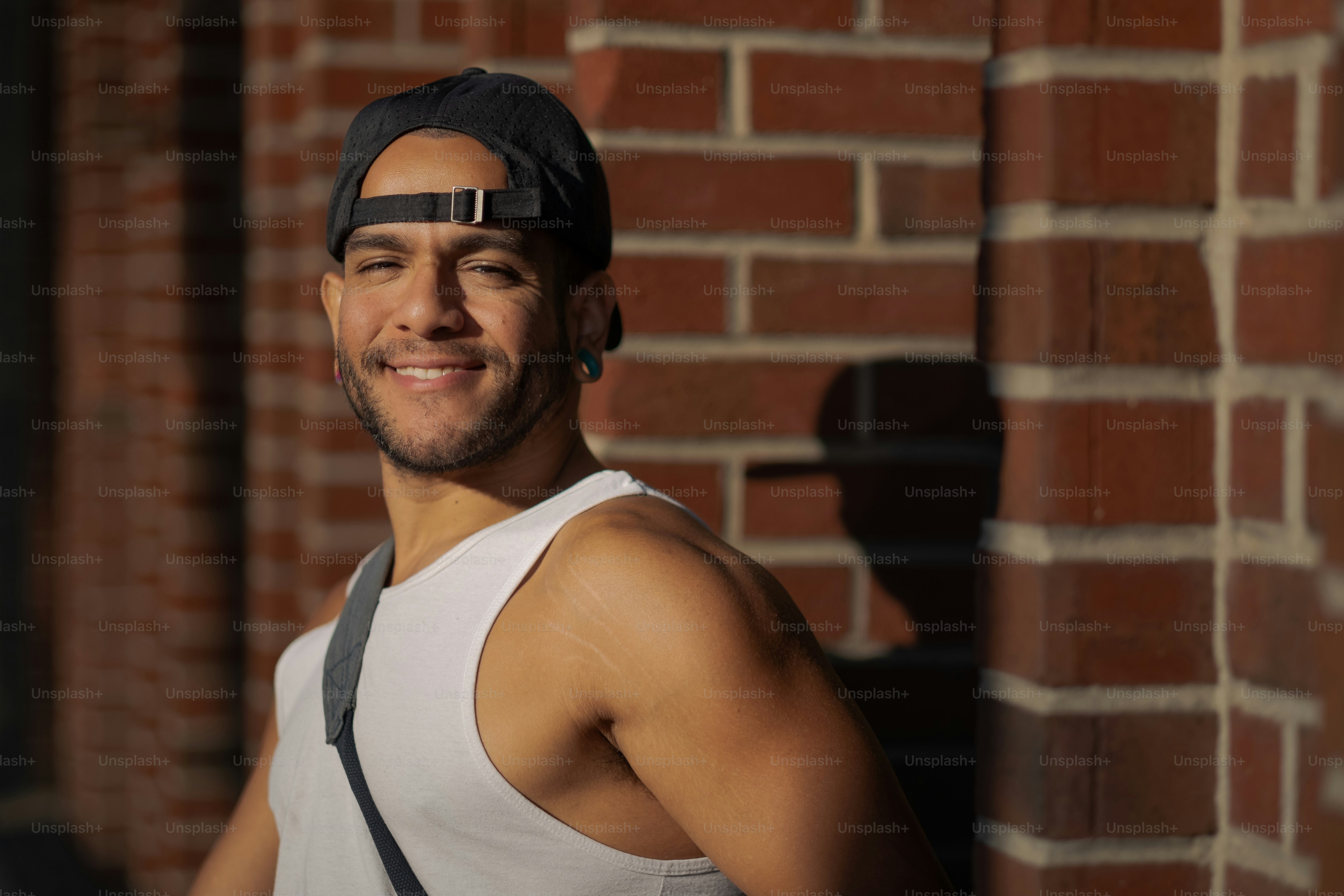 a man in a tank top and suspenders standing in front of a brick wall