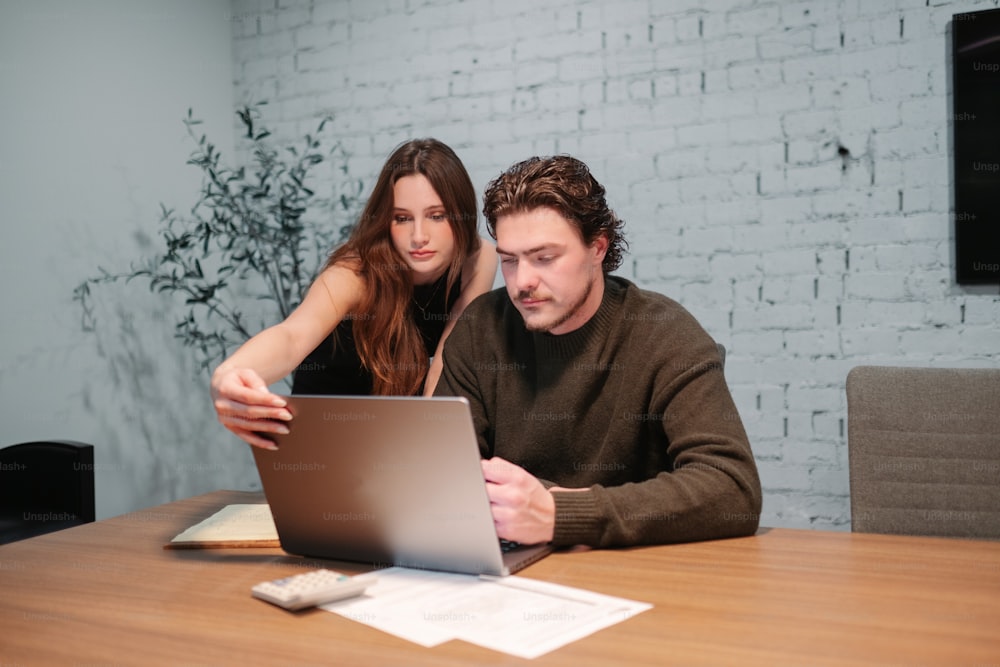 um homem e uma mulher sentados em uma mesa olhando para um laptop