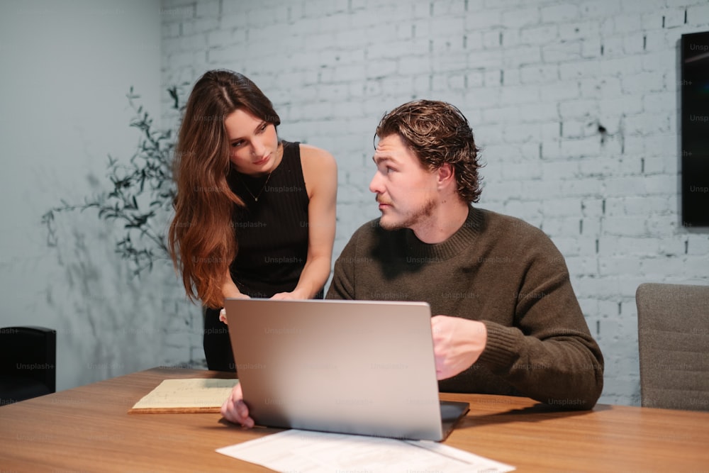 a man and a woman sitting at a table looking at a laptop