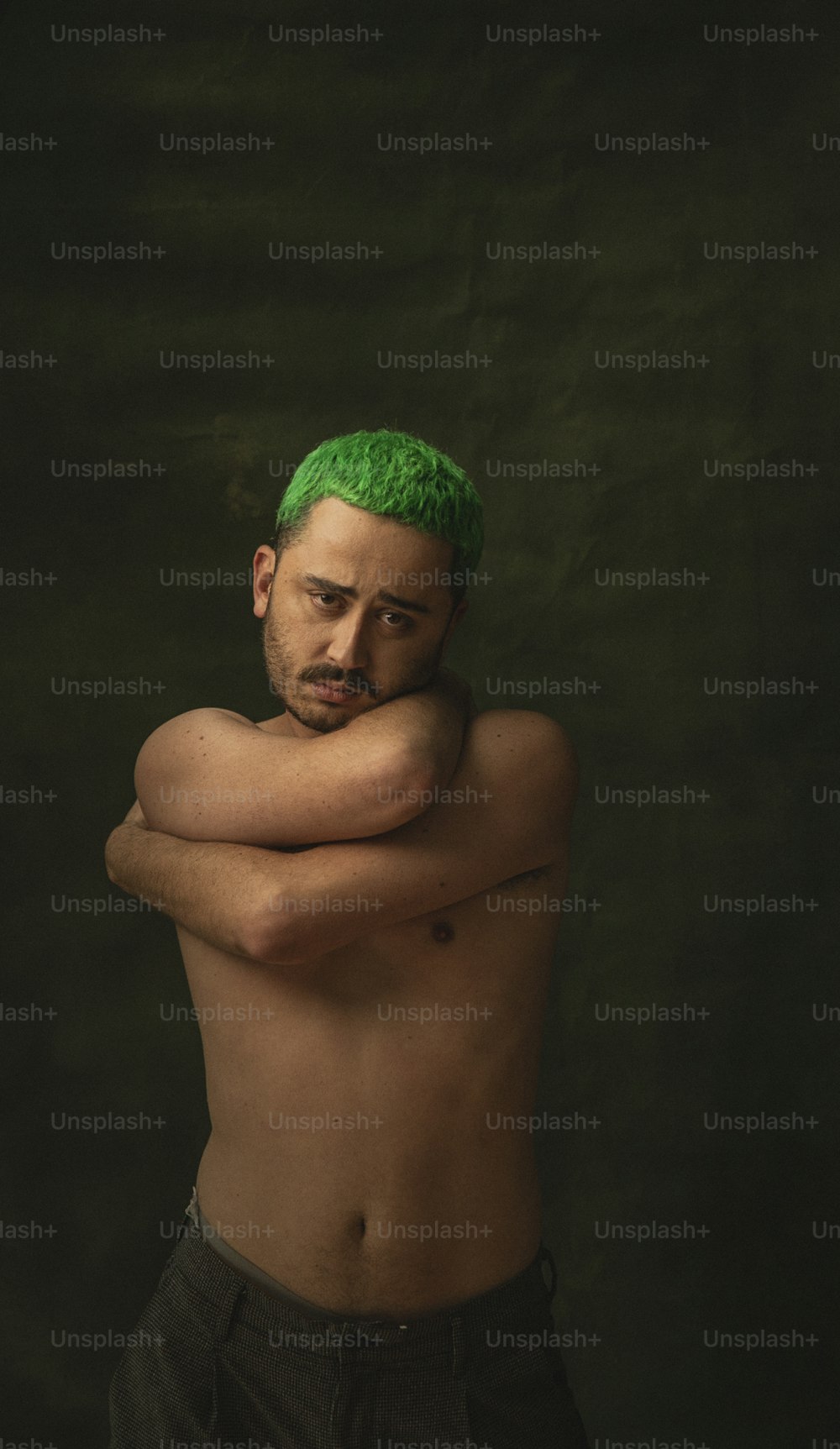 緑の髪の上半身裸の男が写真のポーズをとる