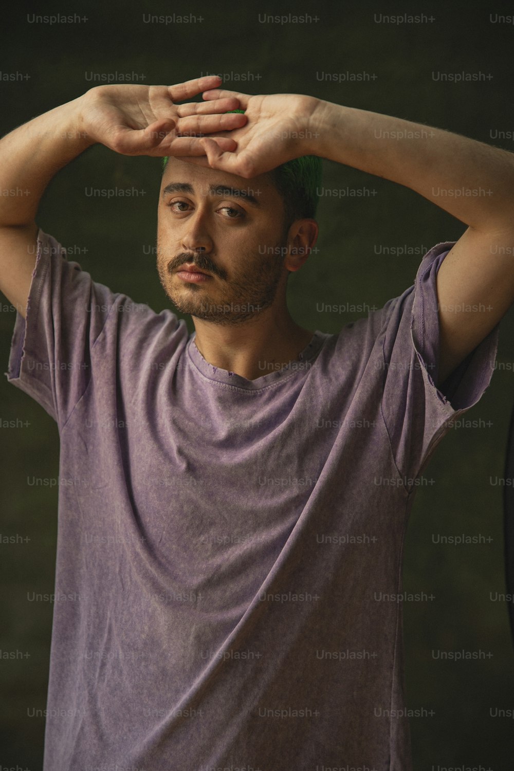 Un hombre con una camisa púrpura sosteniendo sus manos en su cabeza