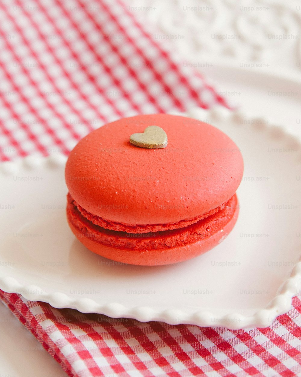 a red macaroon with a gold heart on a white plate