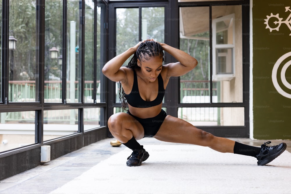 a woman in a black sports bra and shorts squatting on a white floor