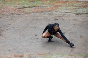 a woman in a black shirt and black pants crouching down on the ground
