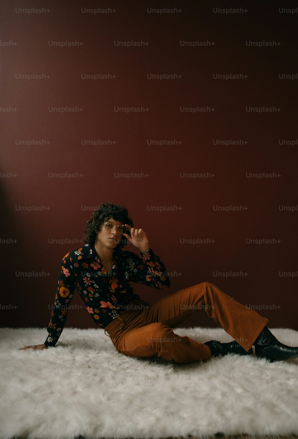 Ein Mann sitzt auf einem weißen Teppich vor einer roten Wand