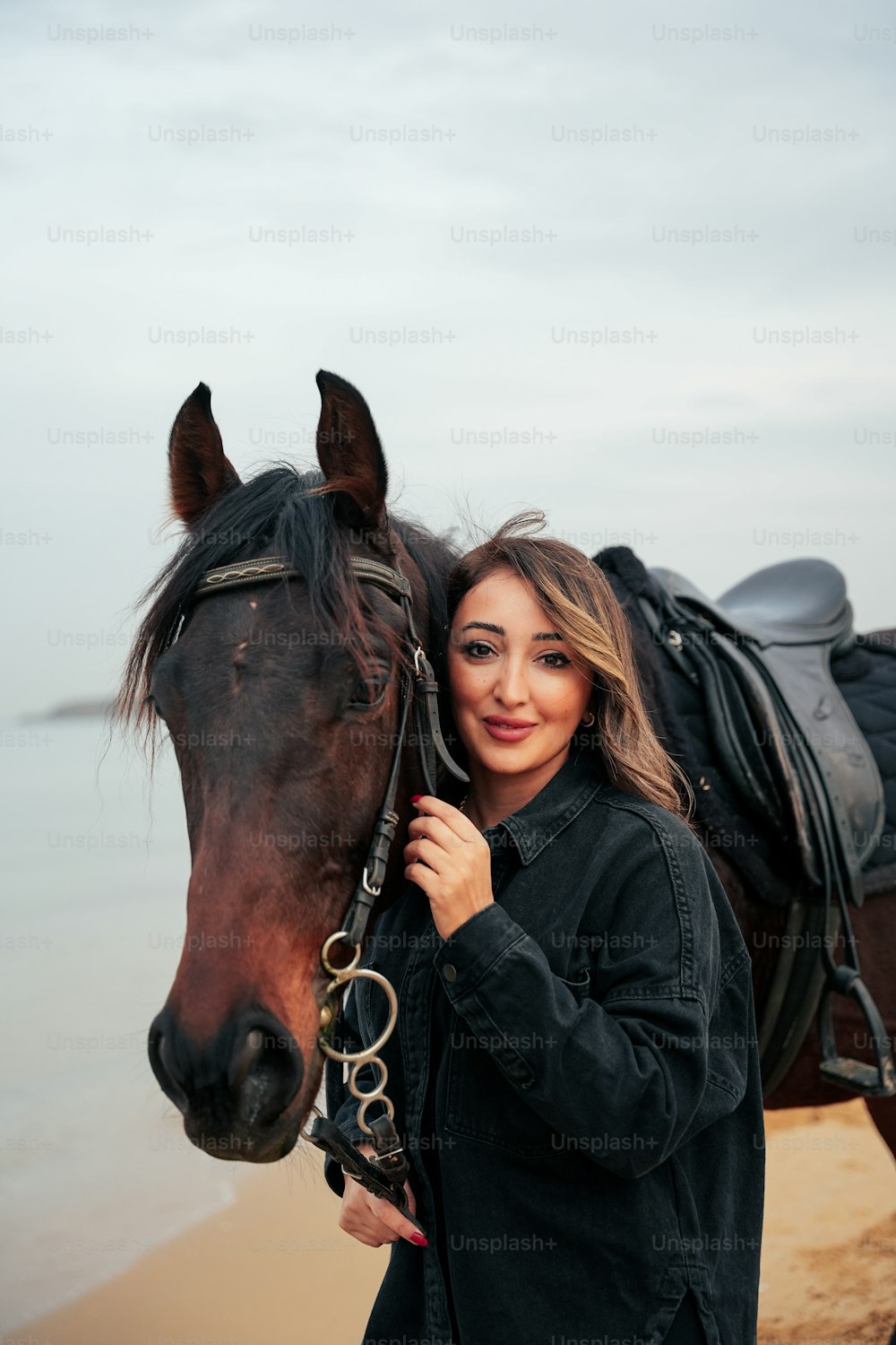 a woman standing next to a horse on a beach