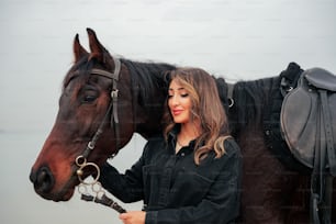 a woman standing next to a brown horse