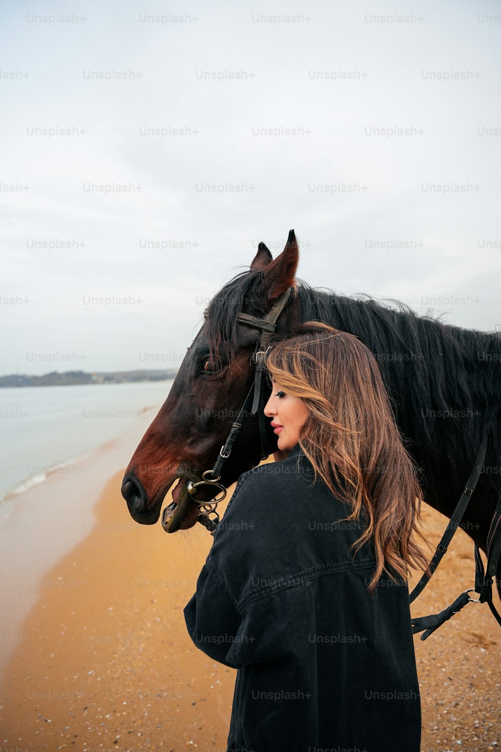 a woman standing next to a horse on a beach