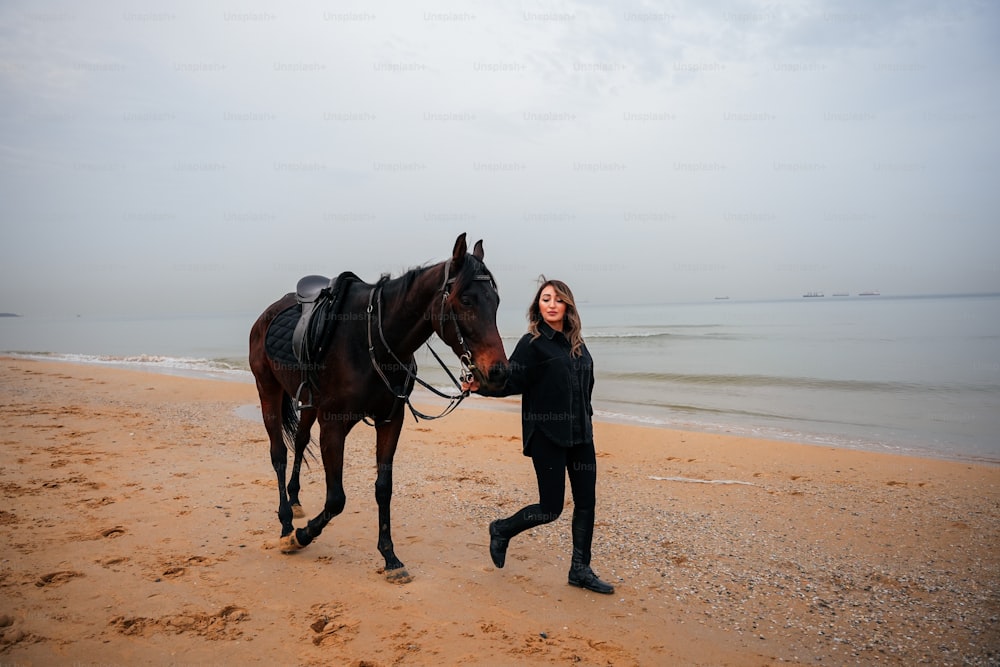 a woman is walking a horse on the beach