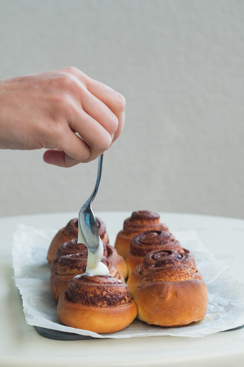 a person is spreading cream on some cinnamon buns
