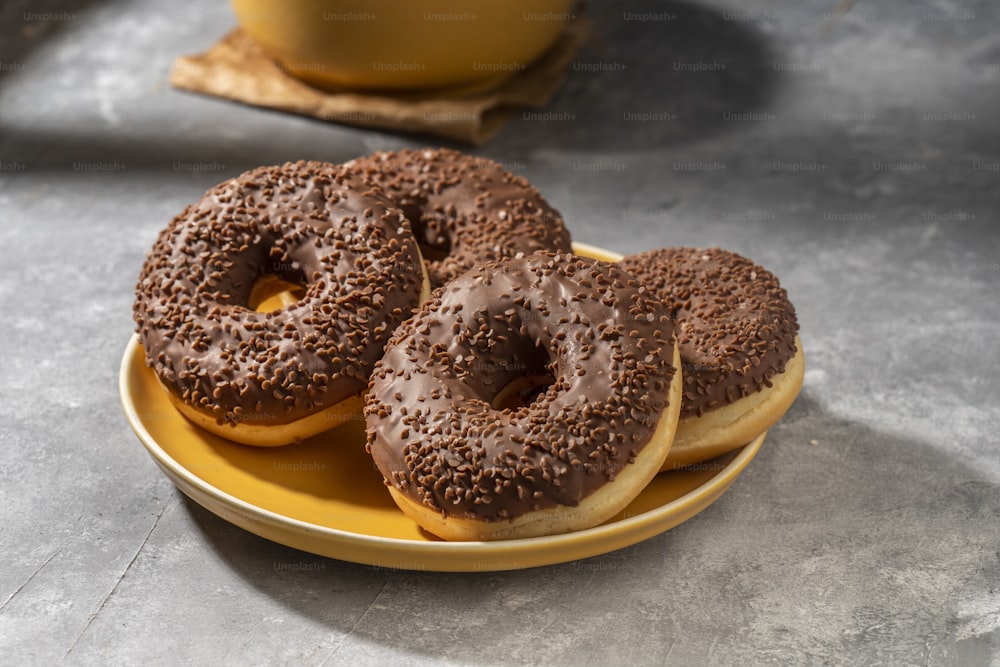 three chocolate donuts sitting on a yellow plate