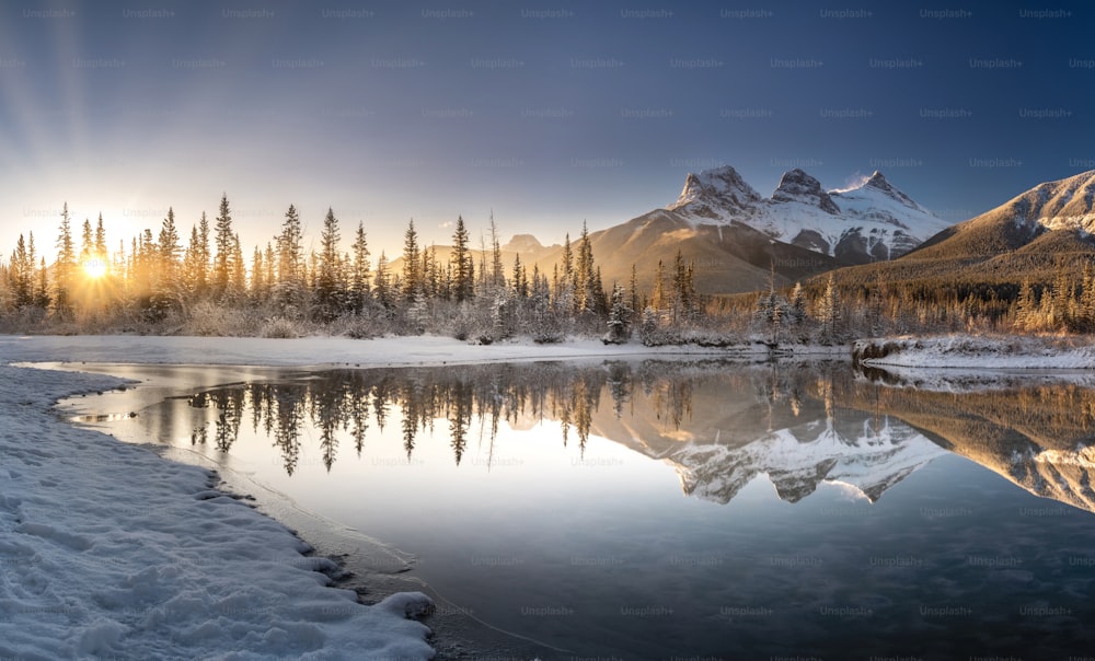 um lago cercado por árvores cobertas de neve e montanhas