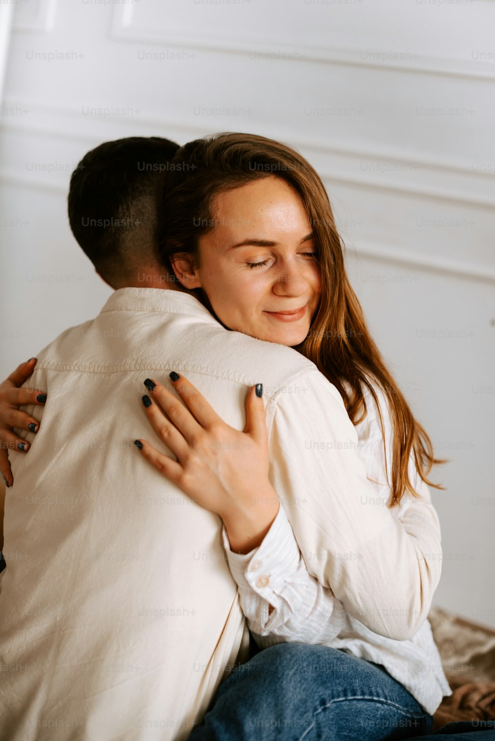 a woman hugging a man who is sitting on a bed
