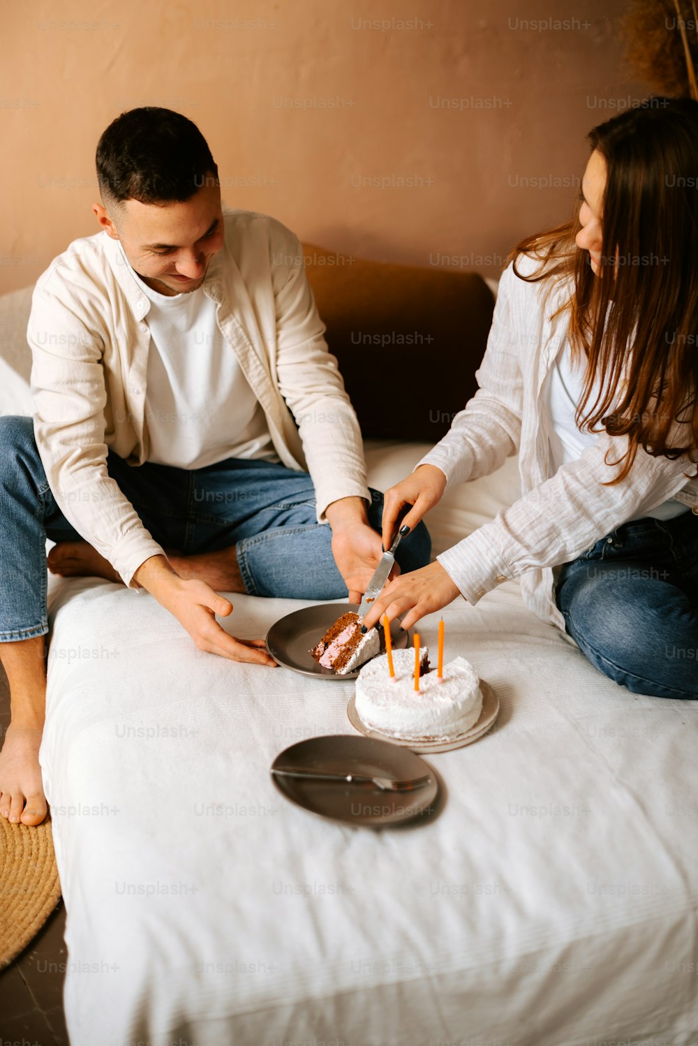 a man and woman sitting on a couch cutting a cake