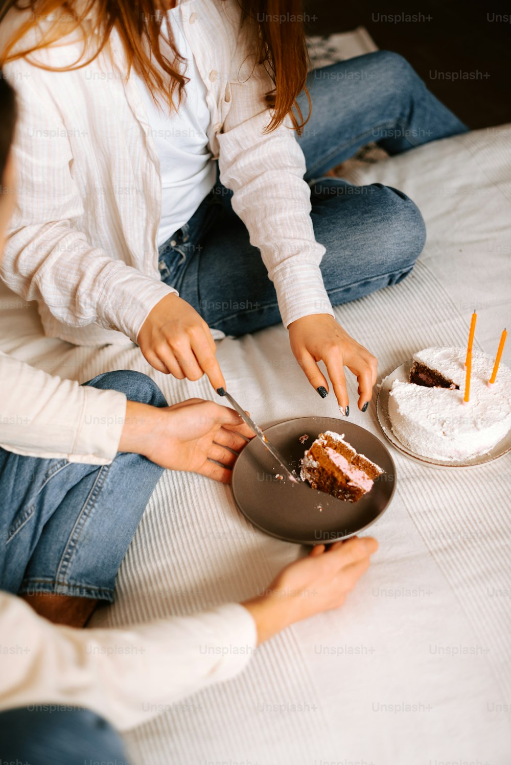 two women sitting on a bed cutting into a cake