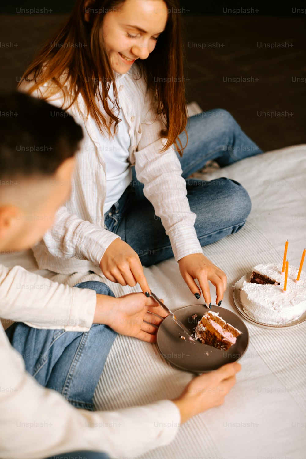 a man and a woman sitting on a bed cutting a cake