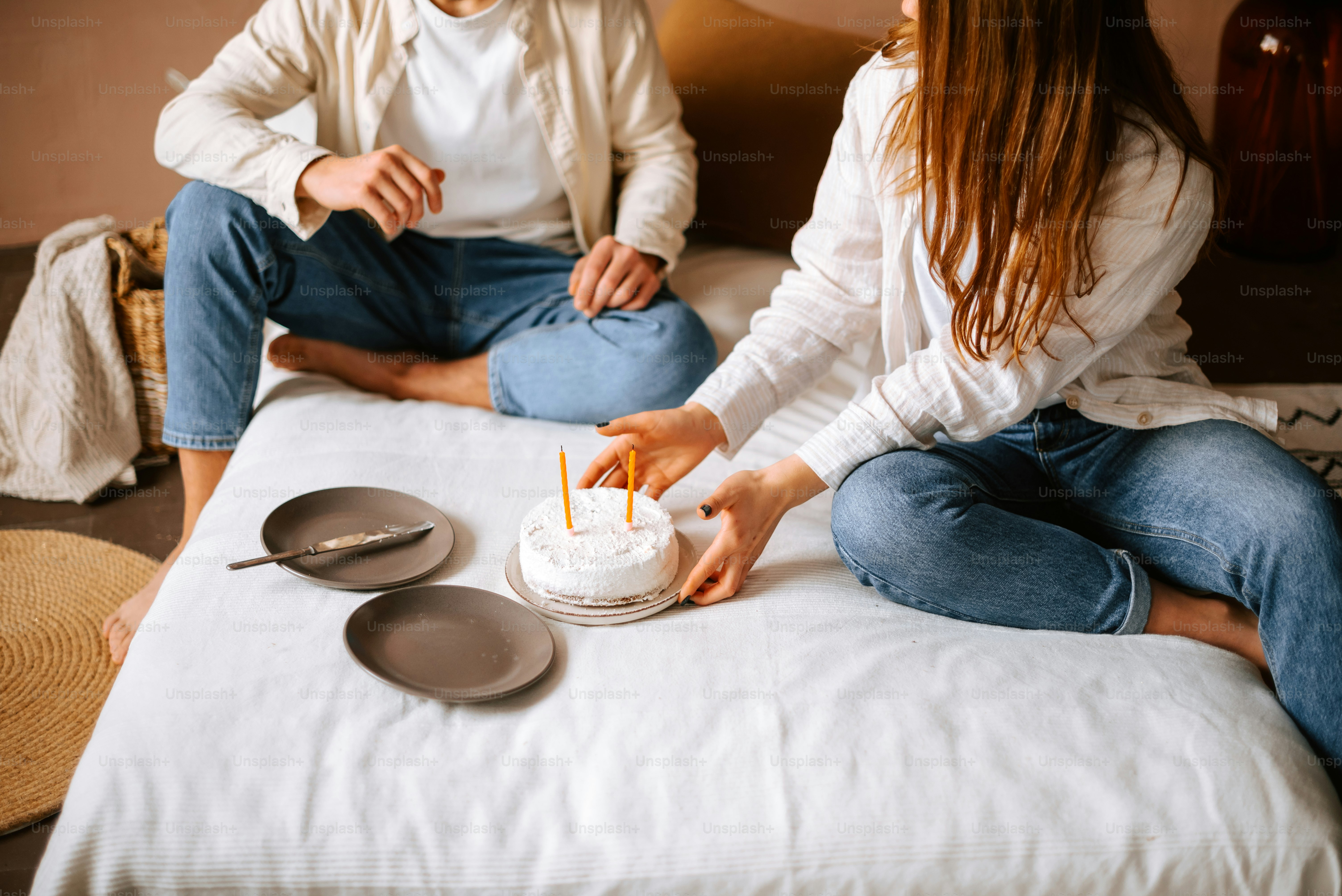 a man and woman sitting on a bed with a cake